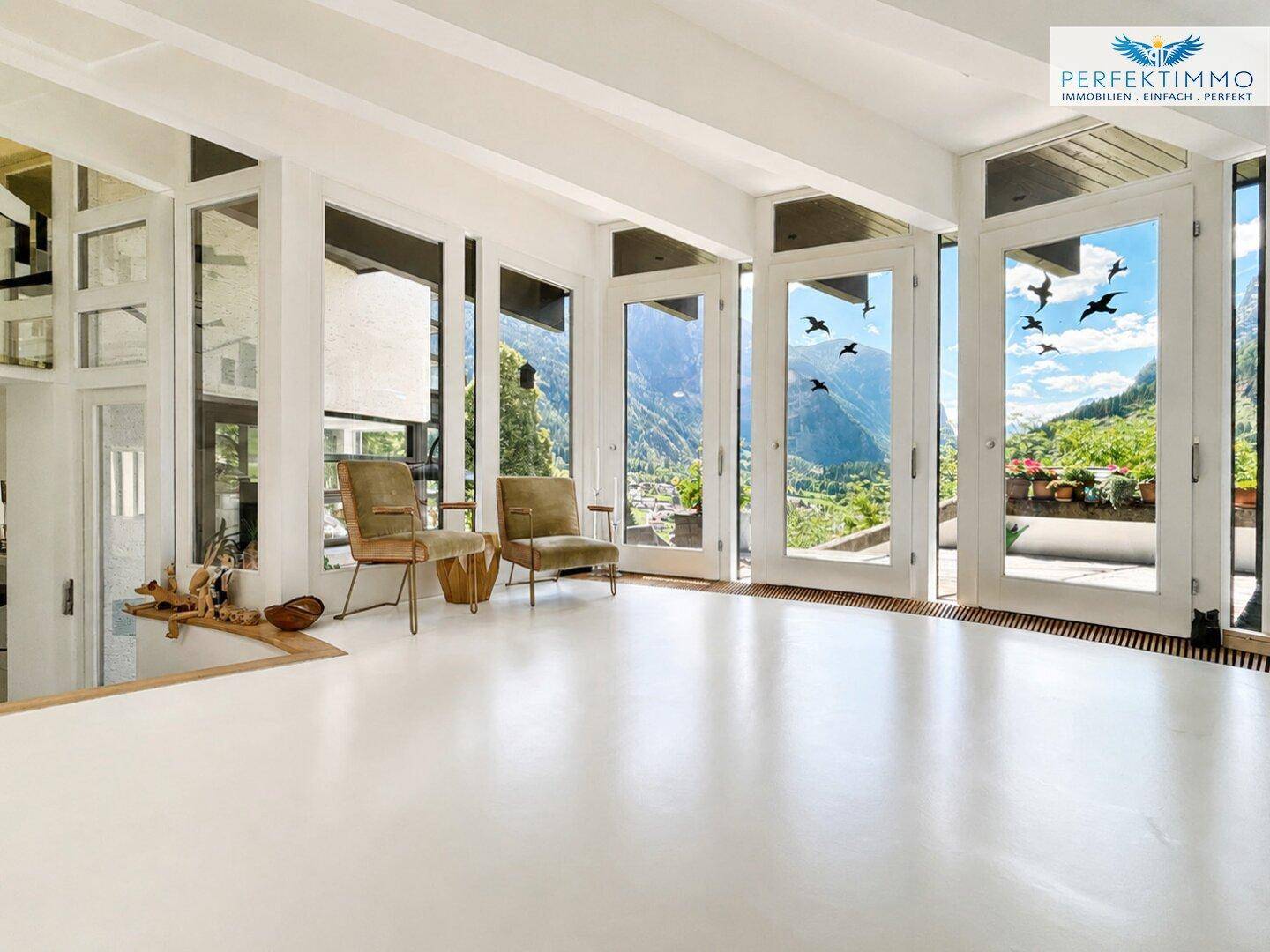 Heller Wohnbereich mit raumhohen Fenstern, die einen Panoramablick auf die Berge bieten.
