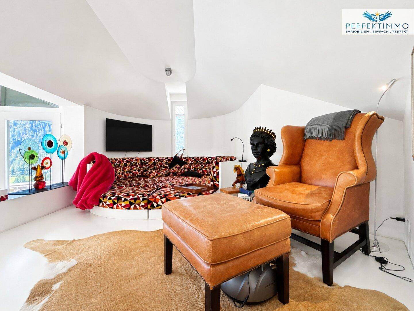 Moderner Wohnbereich mit Ledersessel, farbenfrohem Sofa und Blick auf die Natur.