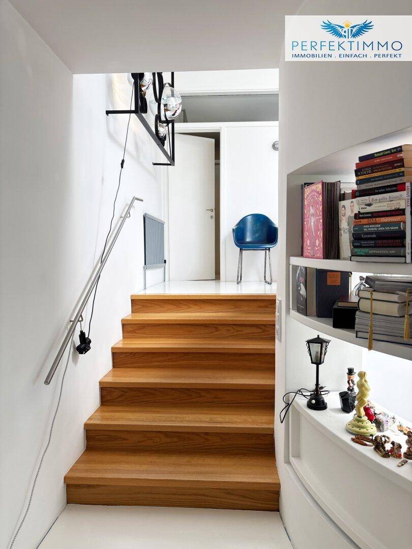 Holztreppe mit modernem Geländer und integriertem Bücherregal in einem hellen Flur.
