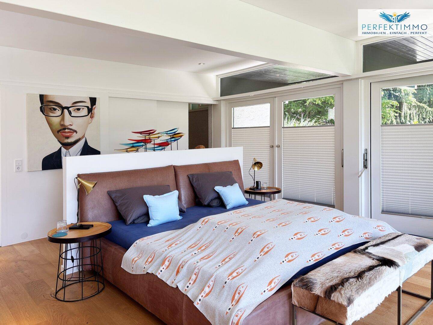 Helles Schlafzimmer mit Lederbett, Holzboden und Zugang zu einem Außenbereich.