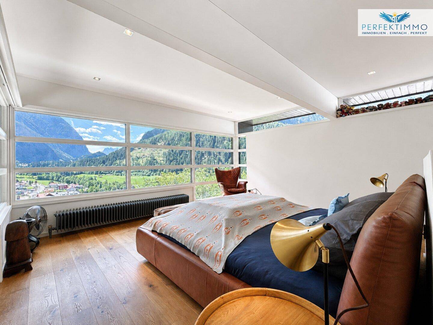 Geräumiges Schlafzimmer mit Lederbett, Holzboden und Panoramablick auf die Berge.