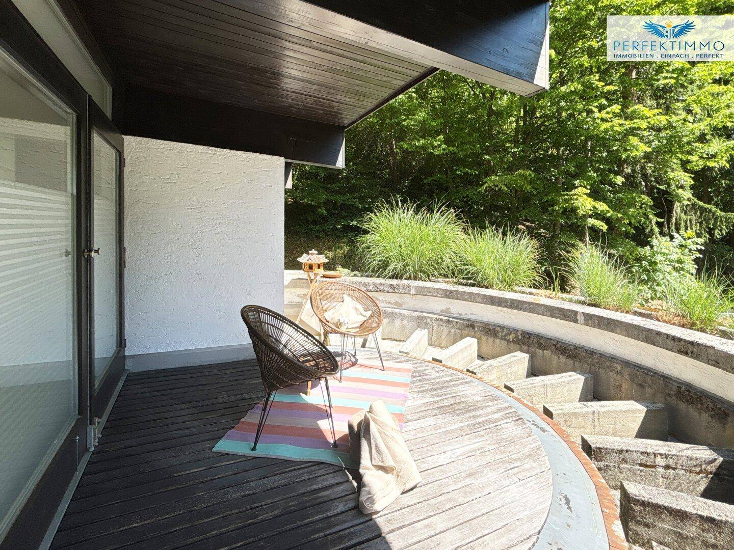 Runde Holzterrasse mit Sitzgelegenheiten und üppiger Vegetation, umgeben von Natur.