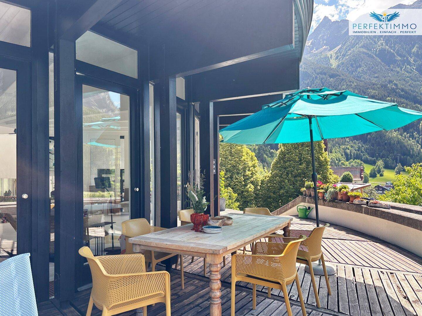 Geräumige Holzterrasse mit Esstisch, Stühlen und Bergblick, ideal für Mahlzeiten im Freien.