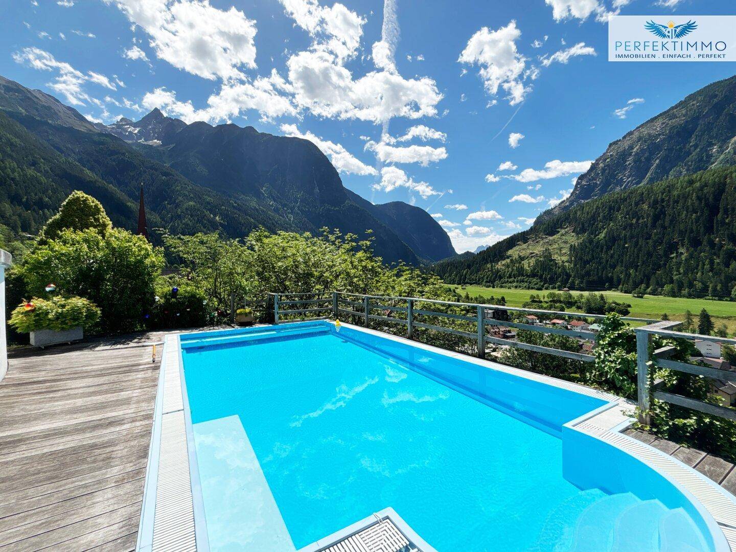 Blauer Pool auf einer Holzterrasse mit Panoramablick auf die umliegenden Berge und das Tal.