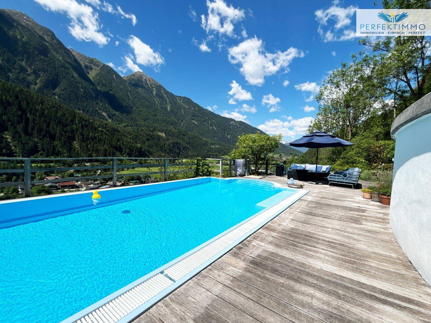 Entspannungsbereich am Pool auf der Holzterrasse mit bequemen Lounge-Möbeln und Bergblick.