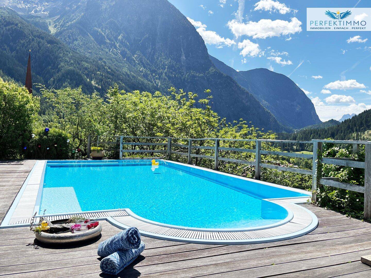 Einladender Poolbereich auf der Holzterrasse mit Handtüchern und weitem Bergblick.