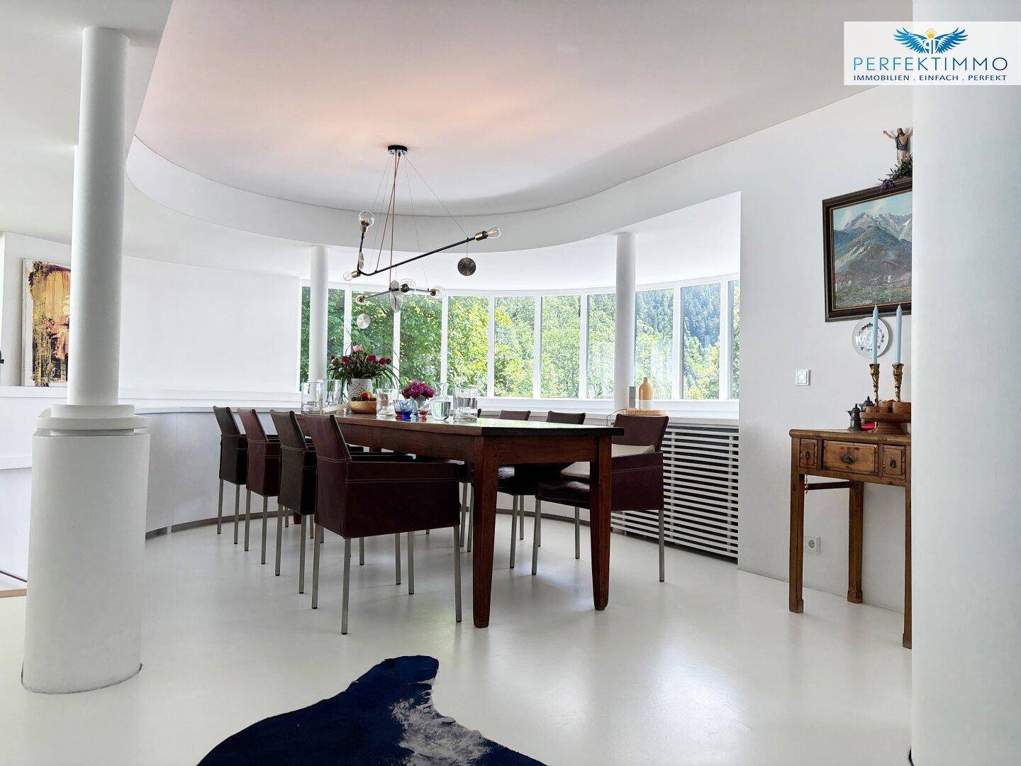 Eleganter Essbereich mit großem Holztisch, bequemen Stühlen und Panoramafenstern zur Natur.