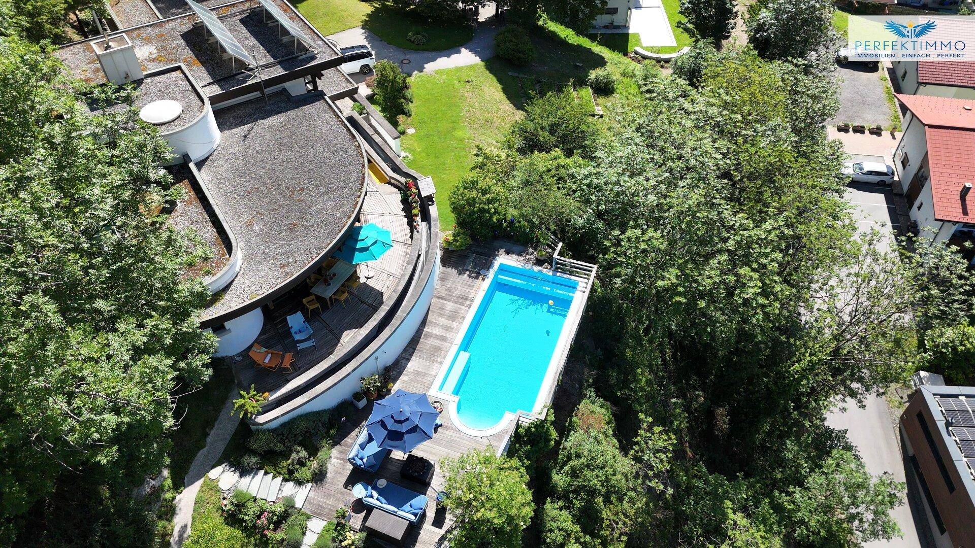 Luftaufnahme der modernen Villa mit Pool und weitläufiger Holzterrasse inmitten grüner Natur.