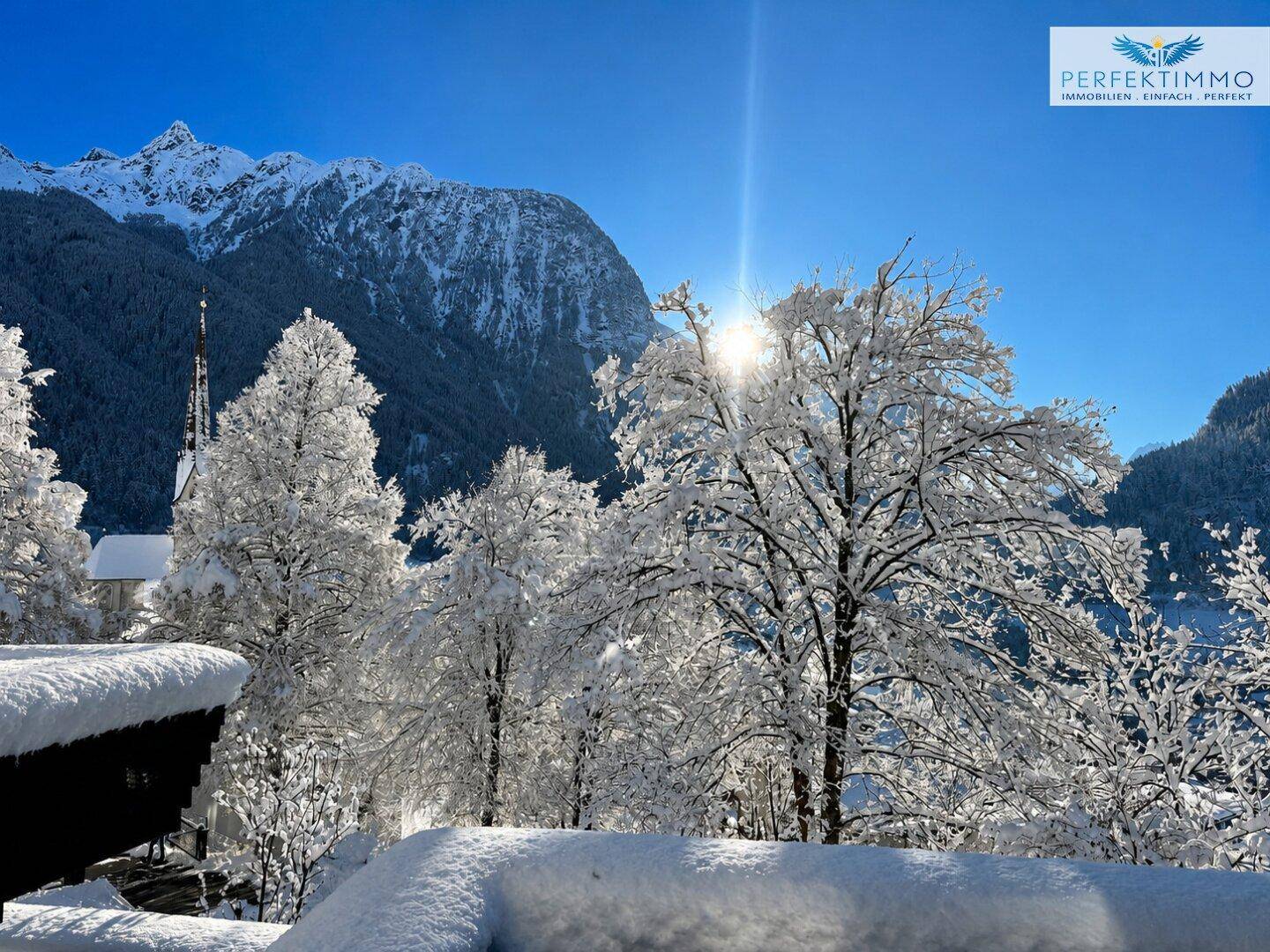 Winterliche Berglandschaft mit schneebedeckten Bäumen und strahlendem Sonnenschein.