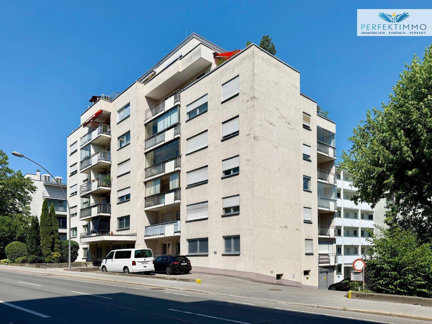 Mehrstöckiges Wohngebäude mit mehreren Balkonen und großen Fenstern an einer Straße.