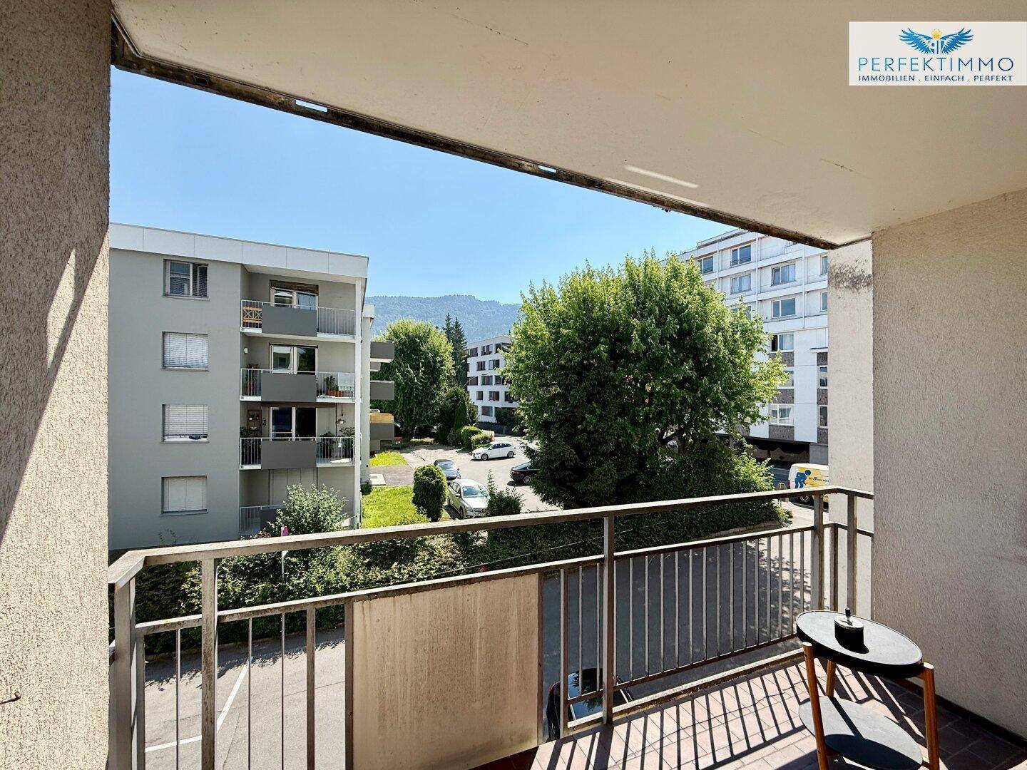 Balkon mit Blick auf die umliegenden Gebäude und grüne Bäume unter blauem Himmel.