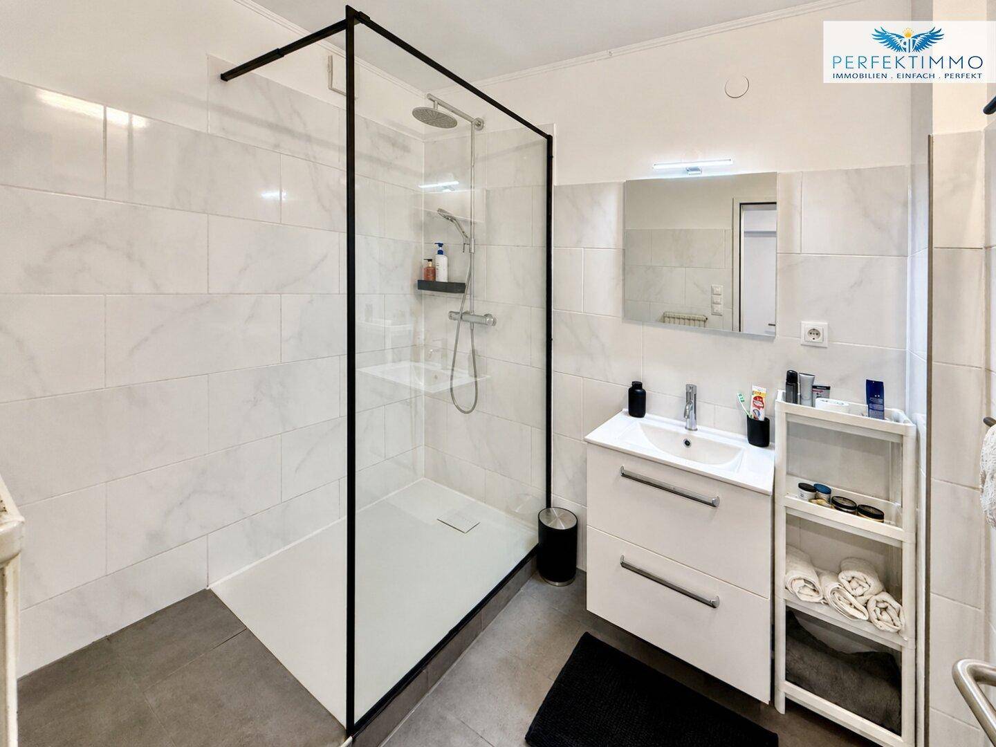 Modernes Badezimmer mit großer begehbarer Dusche, weißen Fliesen und einem Einzelwaschbecken.