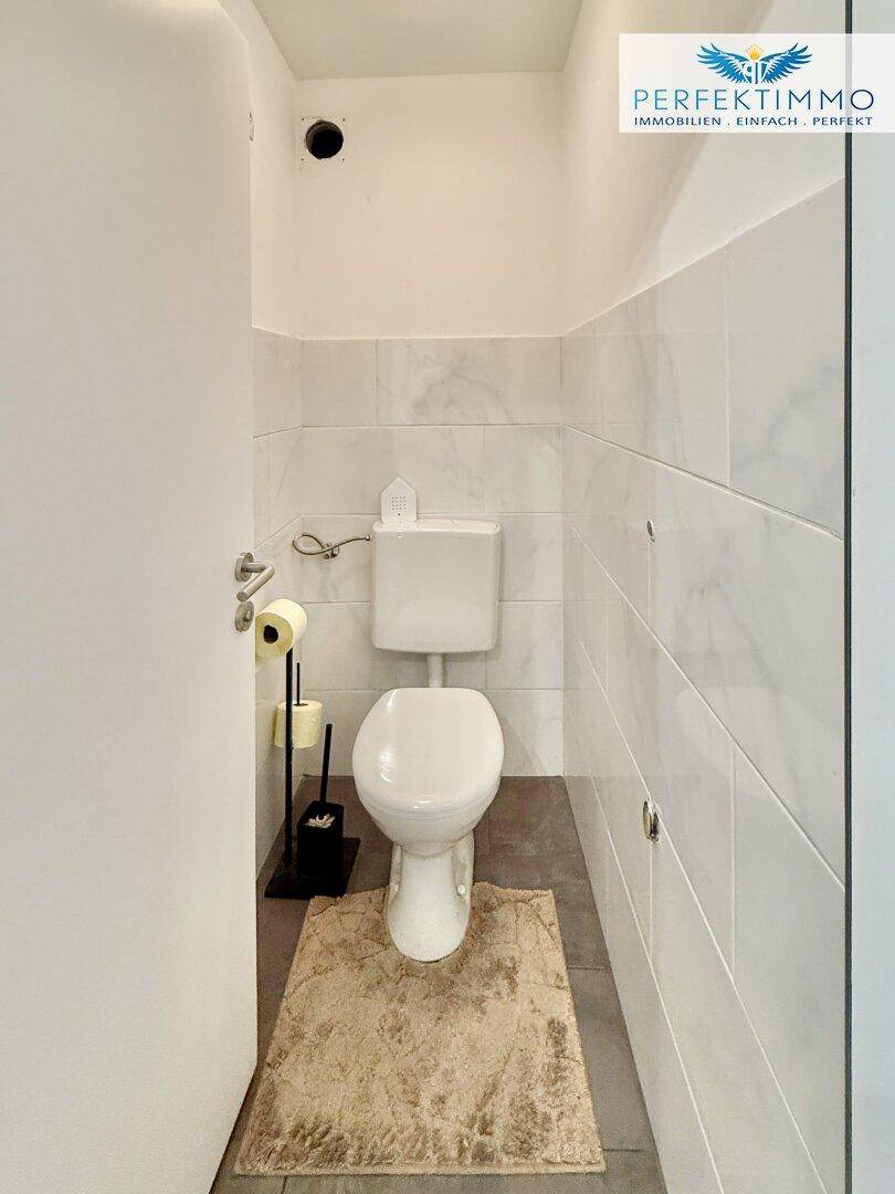 Separate Toilette mit WC und Fliesen an den Wänden, ideal für Gäste.