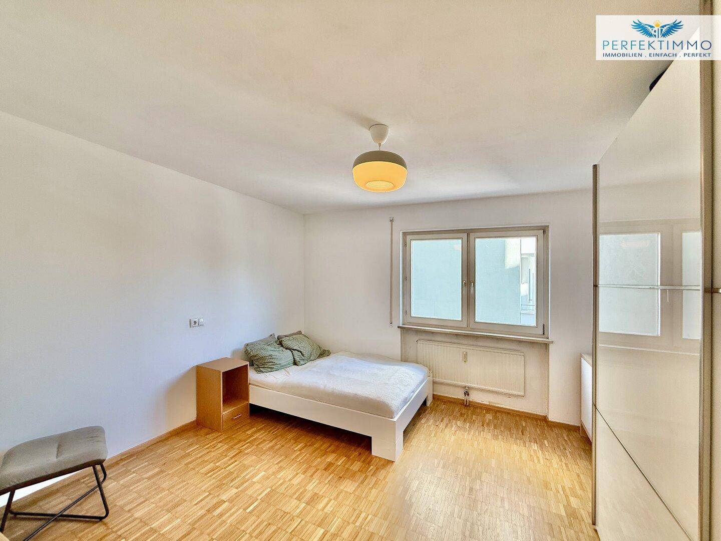 Helles Schlafzimmer mit Parkettboden, einem Bett und einem Fenster mit Ausblick.