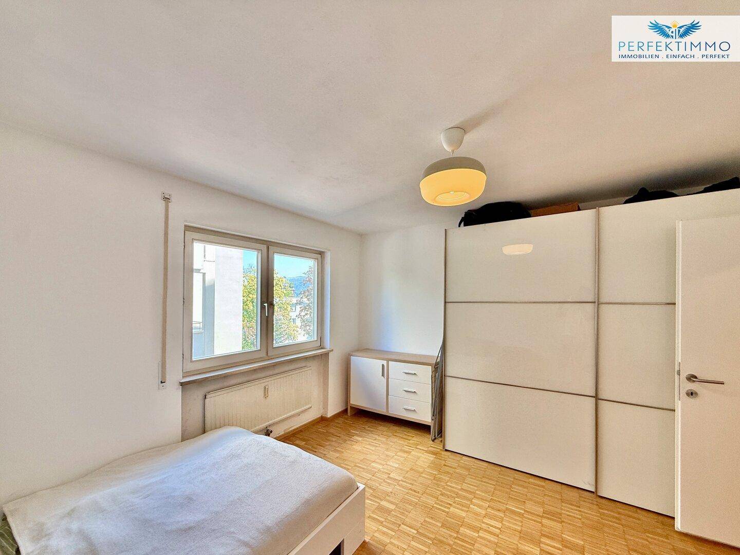 Schlafzimmer mit Parkettboden, großem Kleiderschrank und Fenster mit Blick ins Grüne.