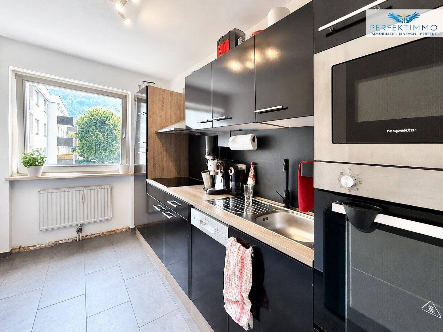 Moderne Küche mit schwarzen Schränken, integrierten Geräten und Fensterblick.