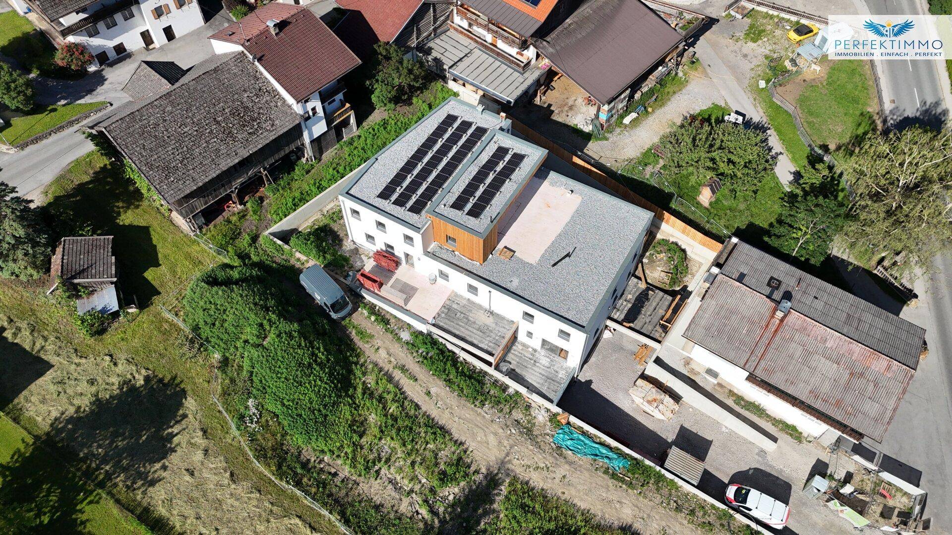 Luftaufnahme eines modernen Gebäudes mit Photovoltaikanlage und grüner Umgebung.