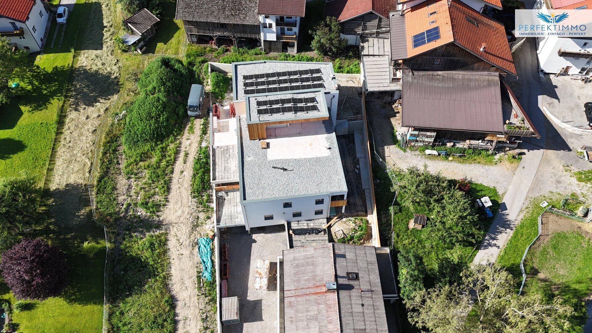 Vogelperspektive einer Wohnanlage mit Photovoltaikanlage und angrenzenden Grundstücken.
