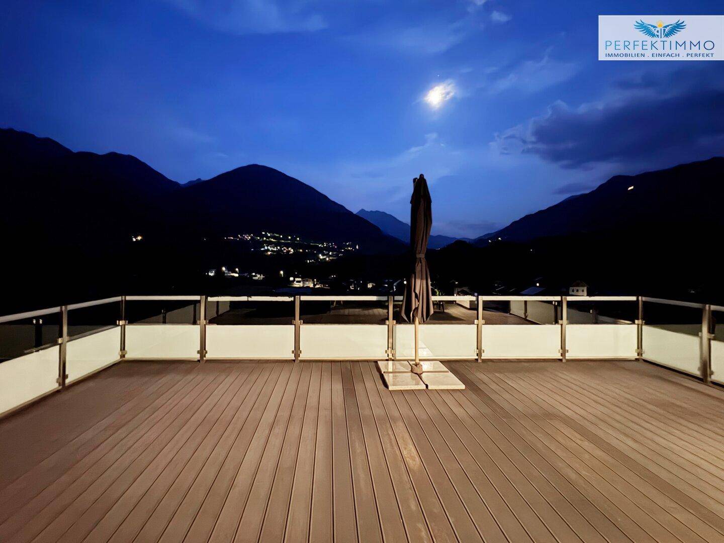 Große Dachterrasse bei Nacht mit Bergblick und stimmungsvoller Beleuchtung, ideal zum Entspannen.