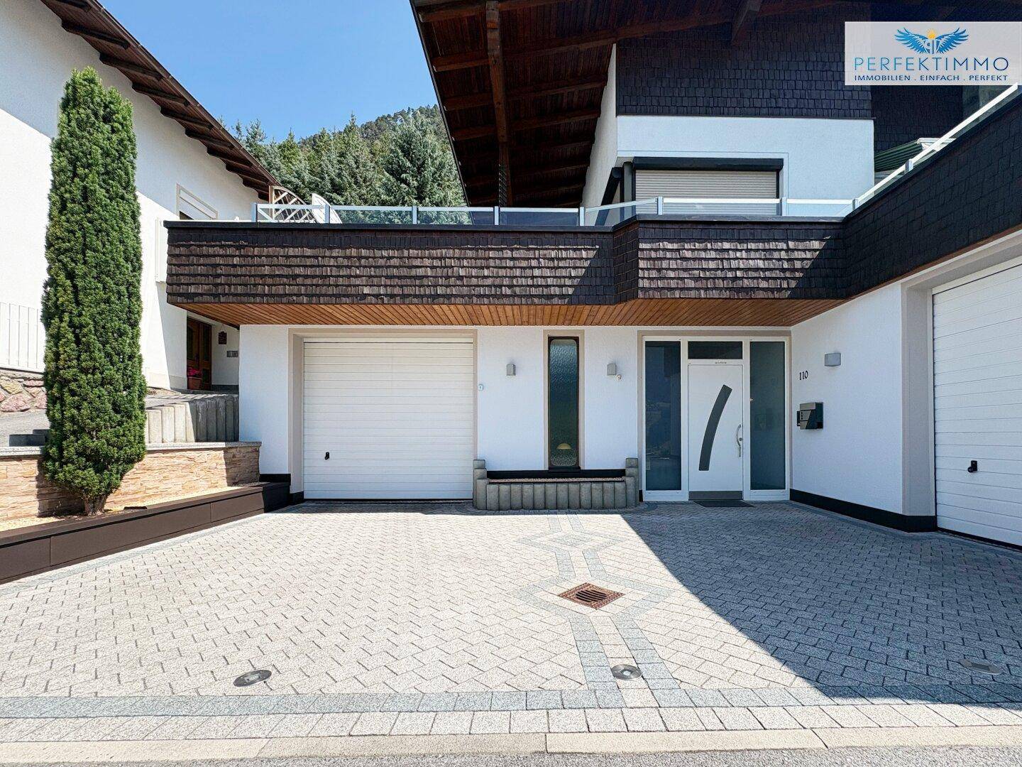 Moderne Hausfassade mit zwei Garagen, gepflasterter Einfahrt und einem einladenden Eingangsbereich.