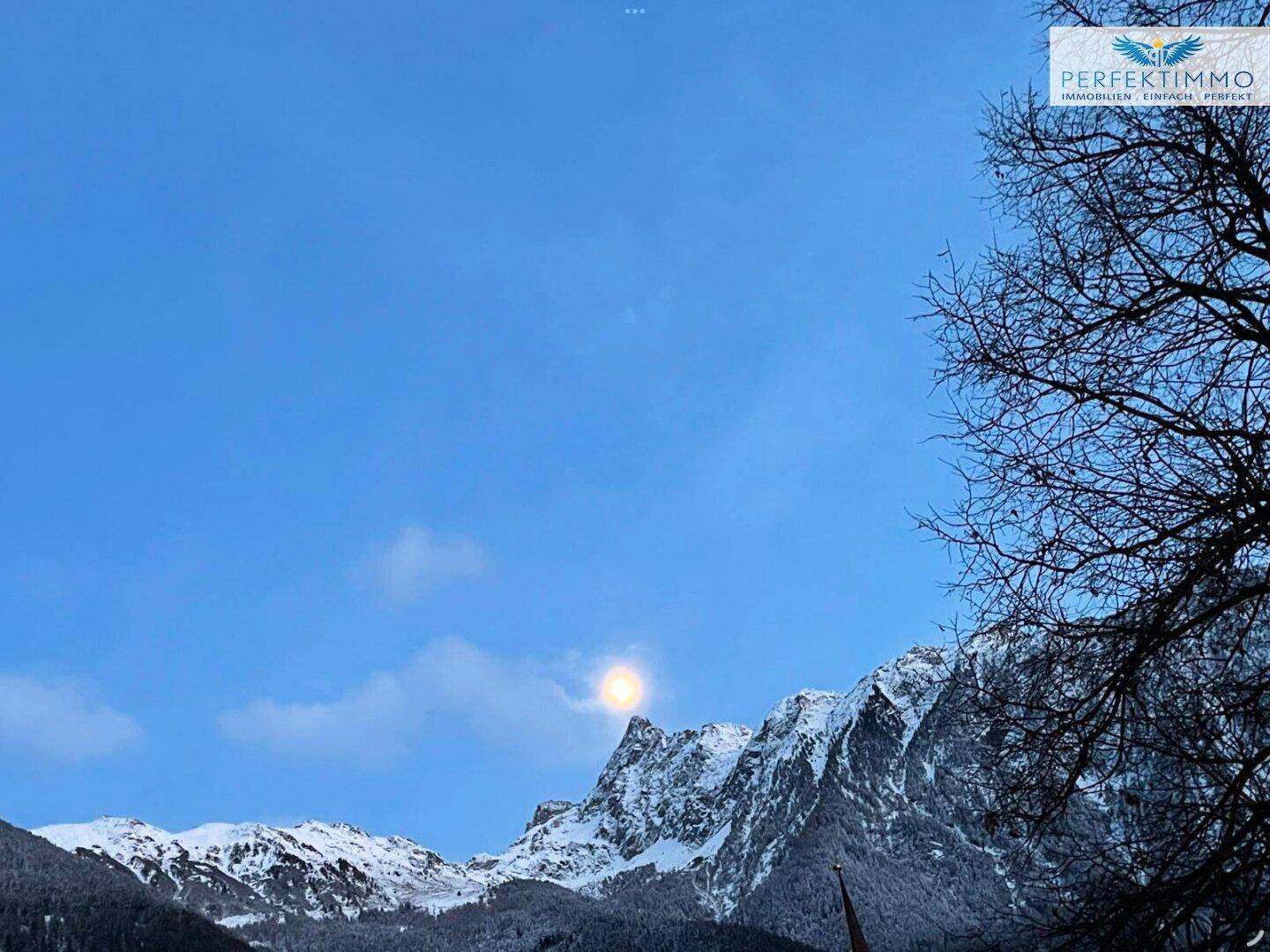 Beeindruckender Vollmond über den schneebedeckten Berggipfeln in der Dämmerung.