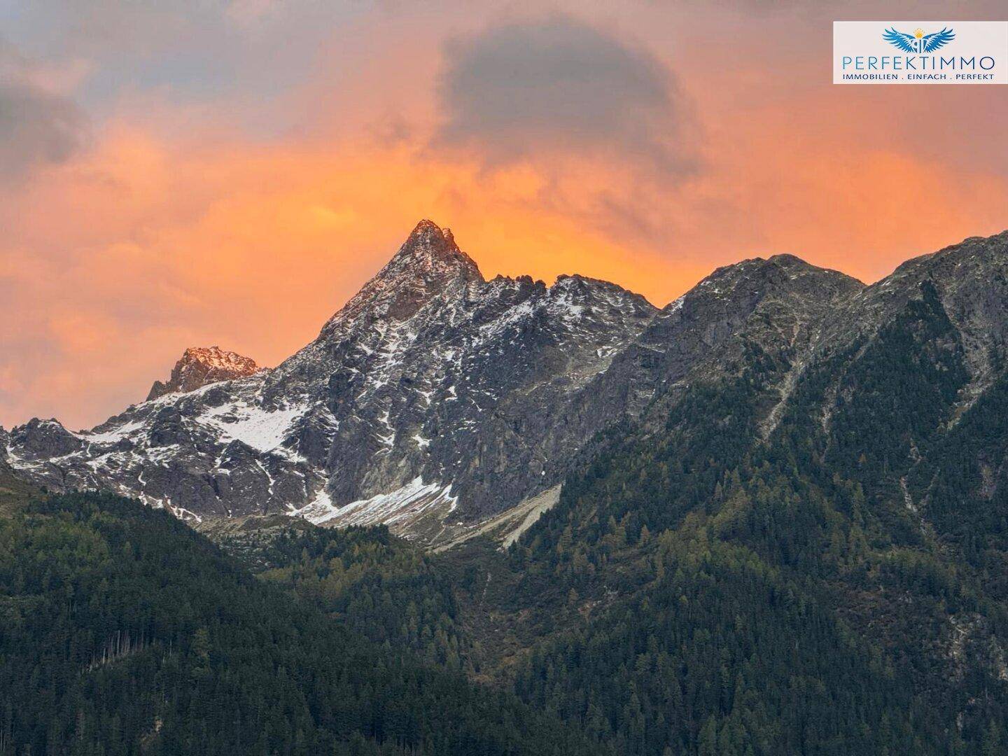 Spektakulärer Sonnenuntergang über den majestätischen Bergen mit bewaldeten Hängen.