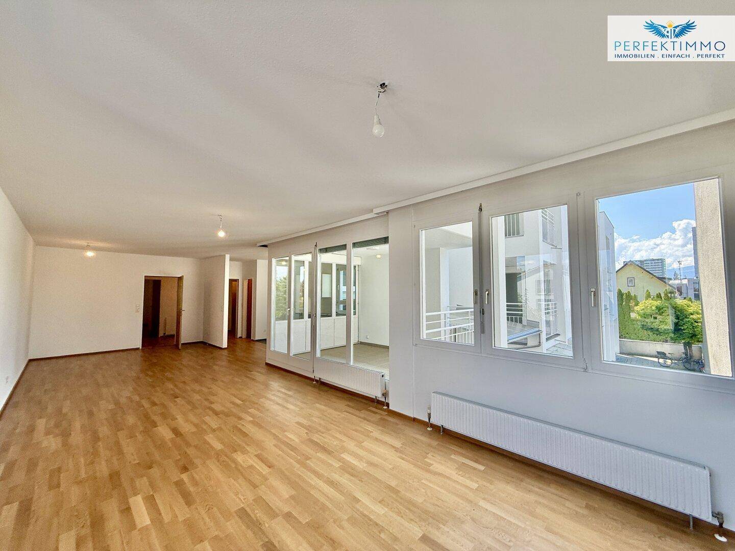 Helles Wohnzimmer mit Parkettboden und weitem Blick durch die großen Fenster auf die Umgebung.