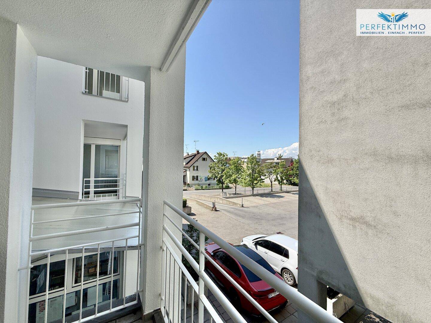 Ausblick vom Balkon auf die Straße und die umliegenden Gebäude mit Bäumen.