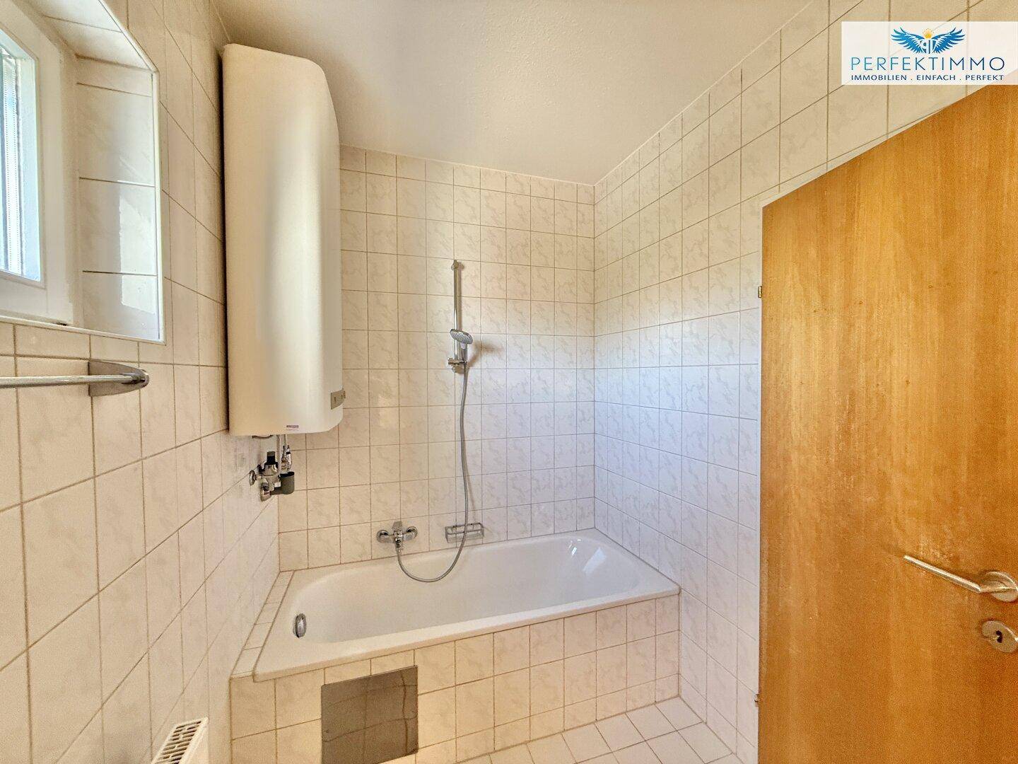 Badezimmer mit Badewanne und Duschvorrichtung, komplett gefliest für einfache Pflege.