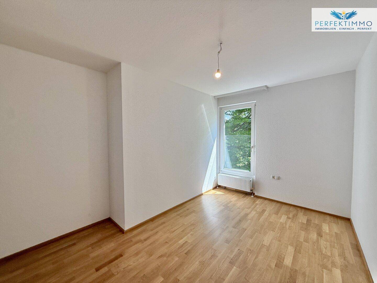 Helles Zimmer mit Parkettboden und einem Fenster, das einen angenehmen Ausblick bietet.