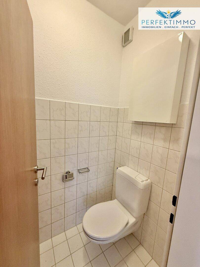 Separates WC mit weißen Fliesen und einer Toilette, funktional und sauber.