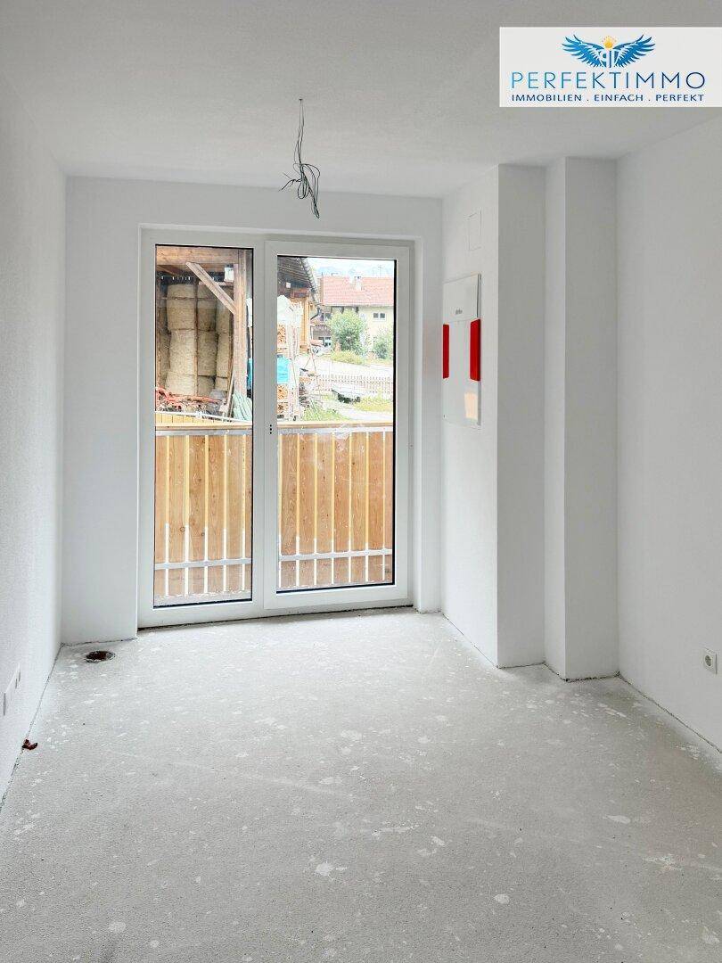 Heller Raum im Rohbau mit Zugang zu einem Balkon, bereit für den Innenausbau.