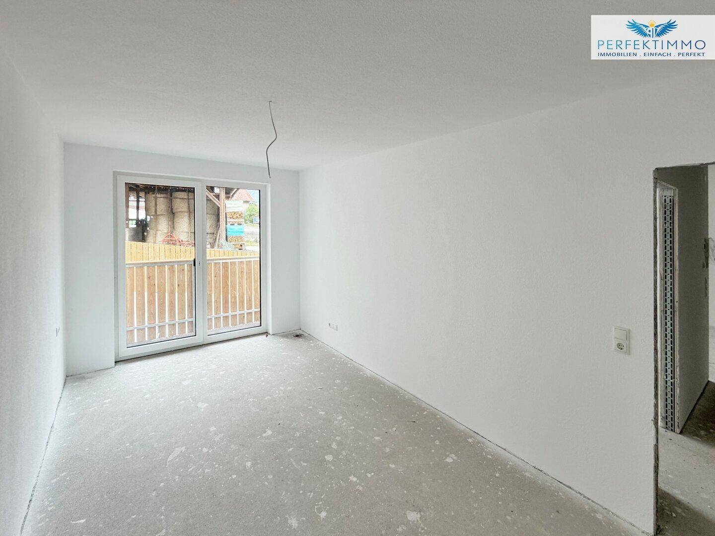 Unfertiger Innenraum mit weiß gestrichenen Wänden und Balkonzugang, viel natürliches Licht.