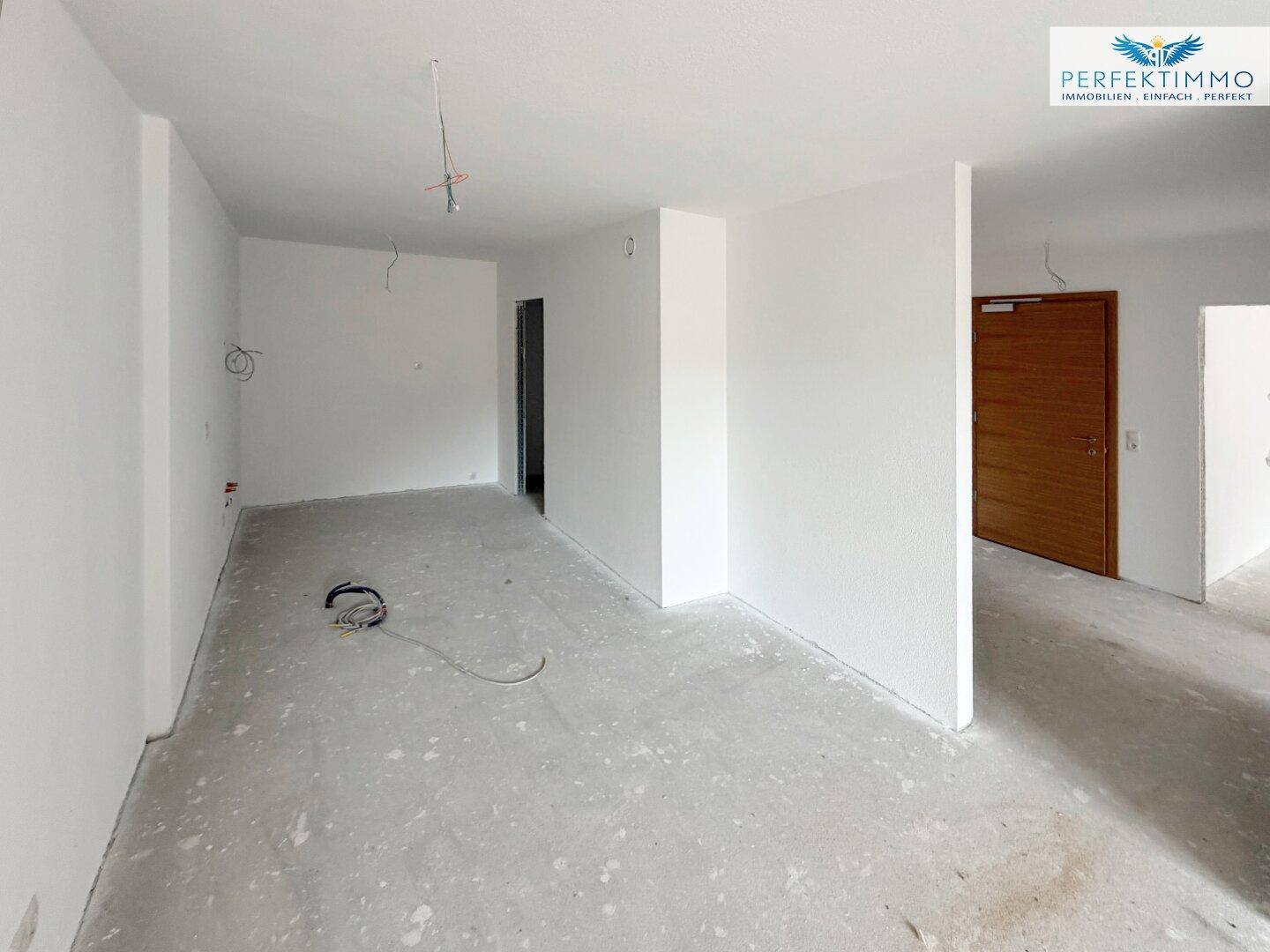 Unfertiger Innenraum mit weißen Wänden und Rohbetonboden, bereit für den Ausbau.