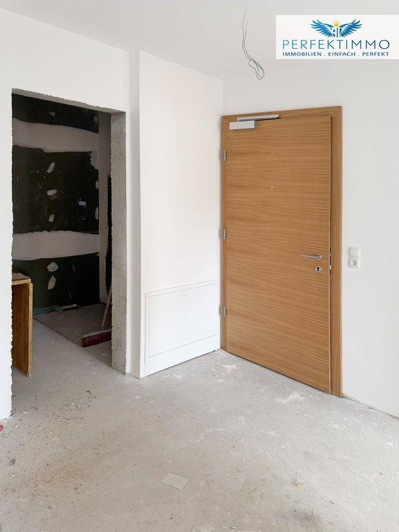 Flur mit Holztür und angrenzendem unfertigen Bereich, bereit für den weiteren Ausbau.