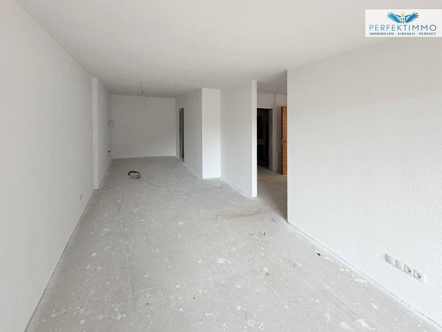 Leerer Raum im Rohbau mit weißen Wänden und unfertigem Boden, wartet auf Fertigstellung.