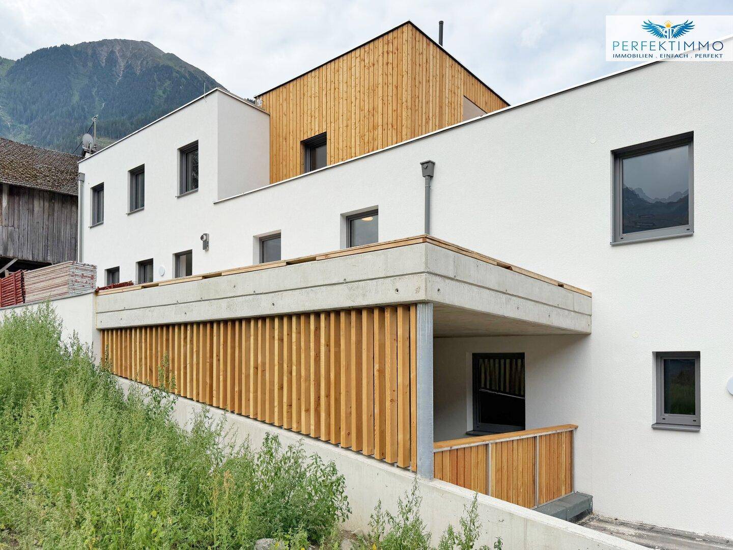Moderne Architektur mit weißer Fassade und Holzverkleidung, integriert in die Berglandschaft.