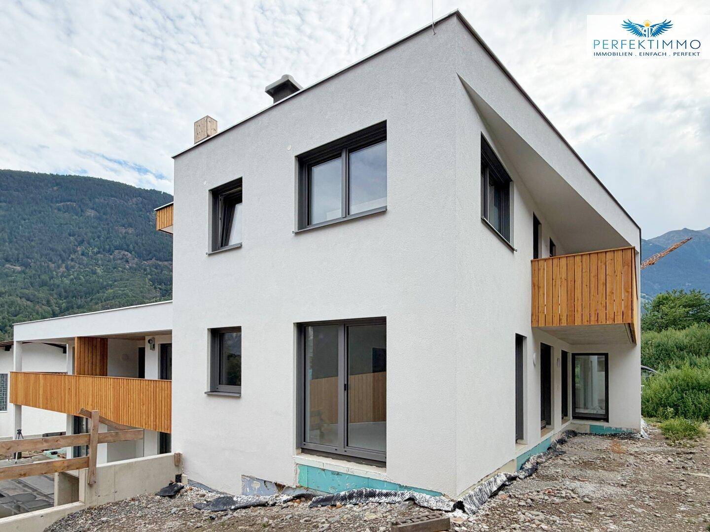 Eckansicht des modernen Neubaus mit großen Fenstern und Holzbalkon in den Bergen.