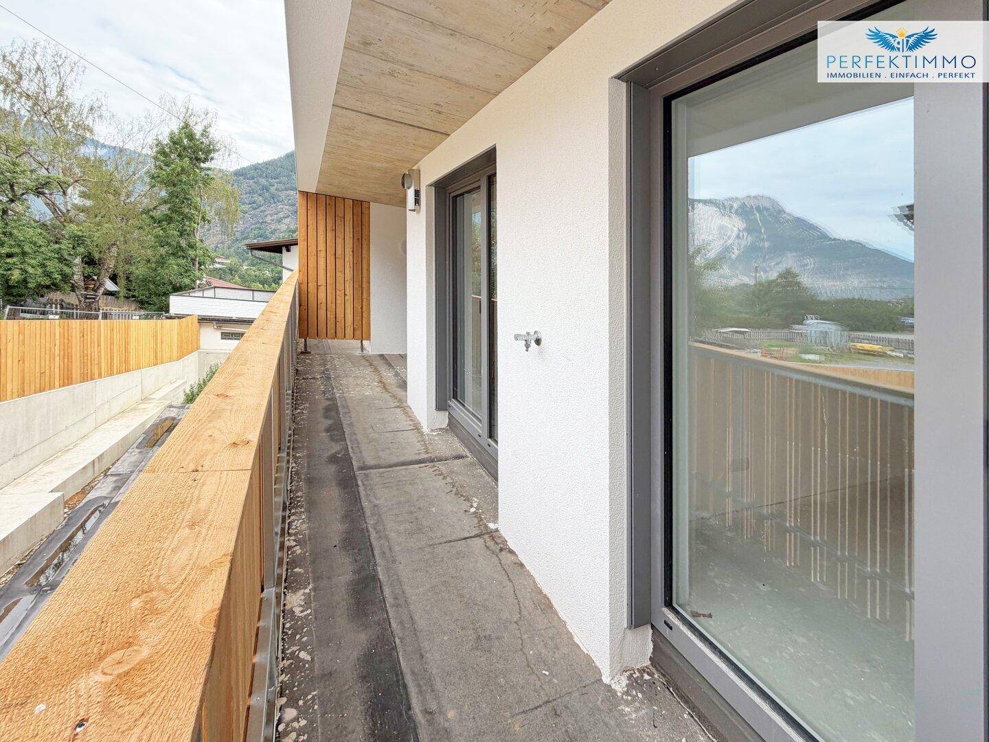 Langer Balkon im Bau mit Holzbalkonbrüstung und Blick auf die umliegende Bergwelt.