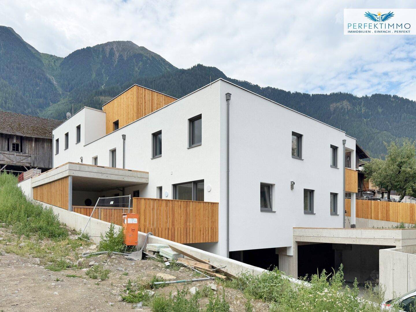 Modernes Gebäude mit weißer Fassade und Holzverkleidung vor einer Bergkulisse.