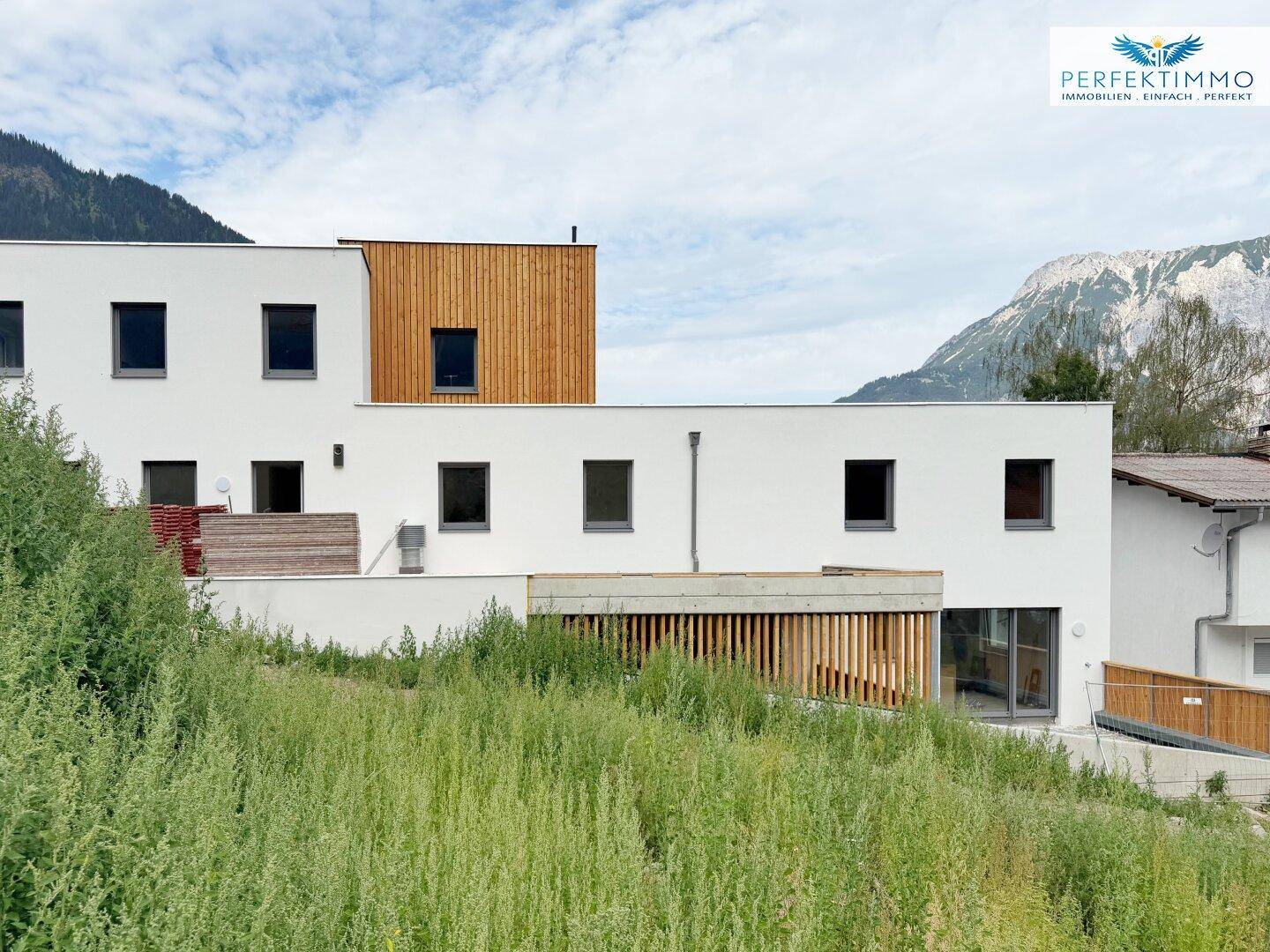 Modernes Wohngebäude mit weißer Putzfassade und Holzdetails in einer bergigen Landschaft.