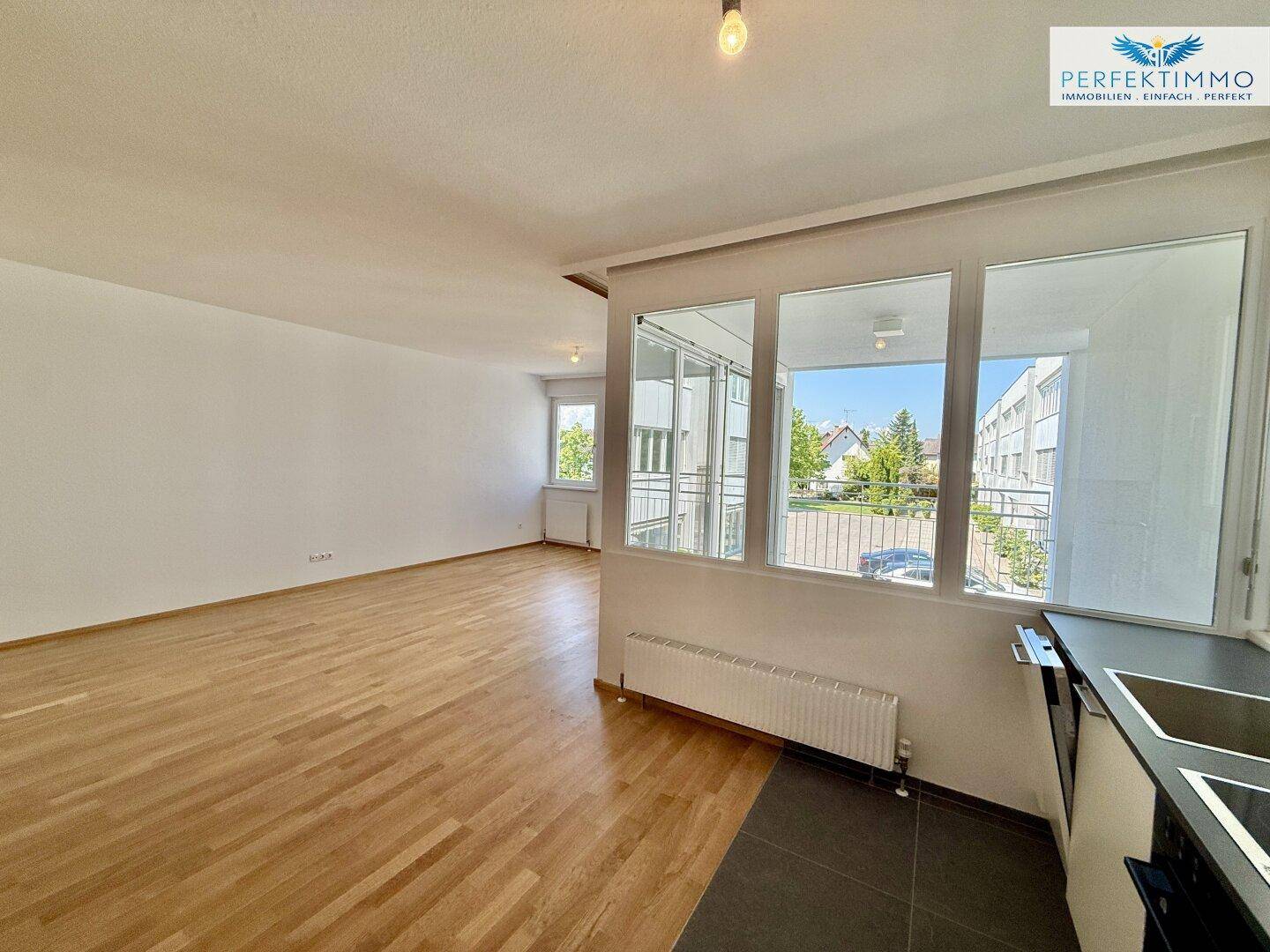 Offener Wohnbereich mit Parkett und Fliesen, Blick auf die Loggia und die Umgebung.