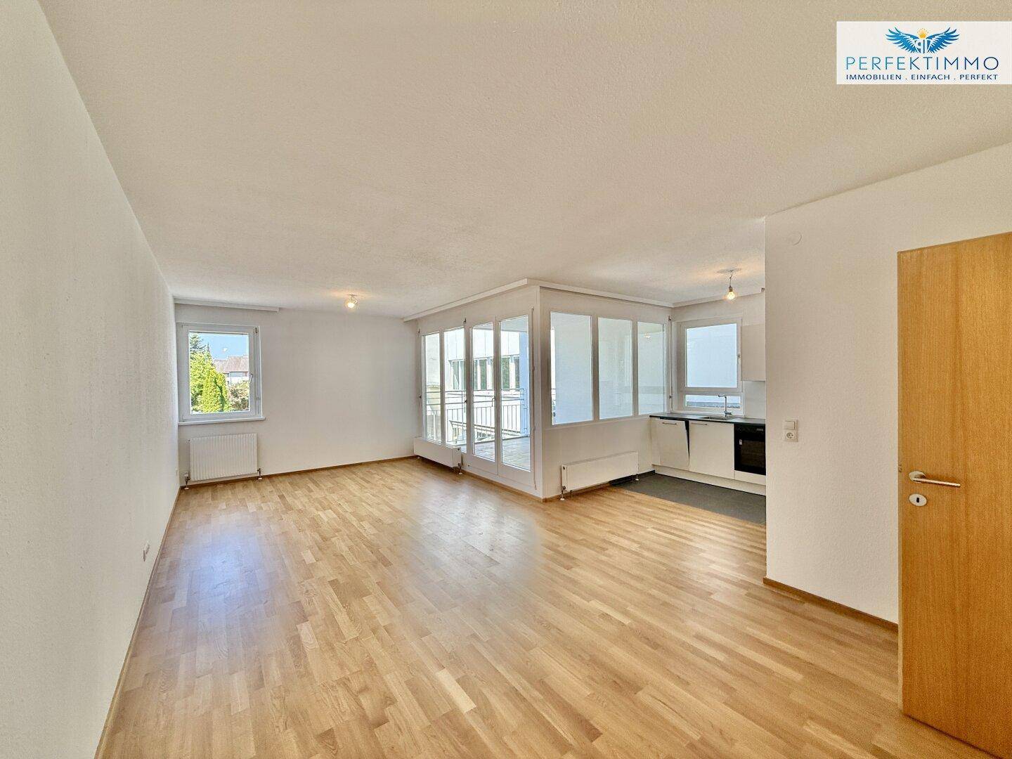 Heller Wohnbereich mit Parkettboden, integrierter Küchenzeile und Zugang zur Loggia.