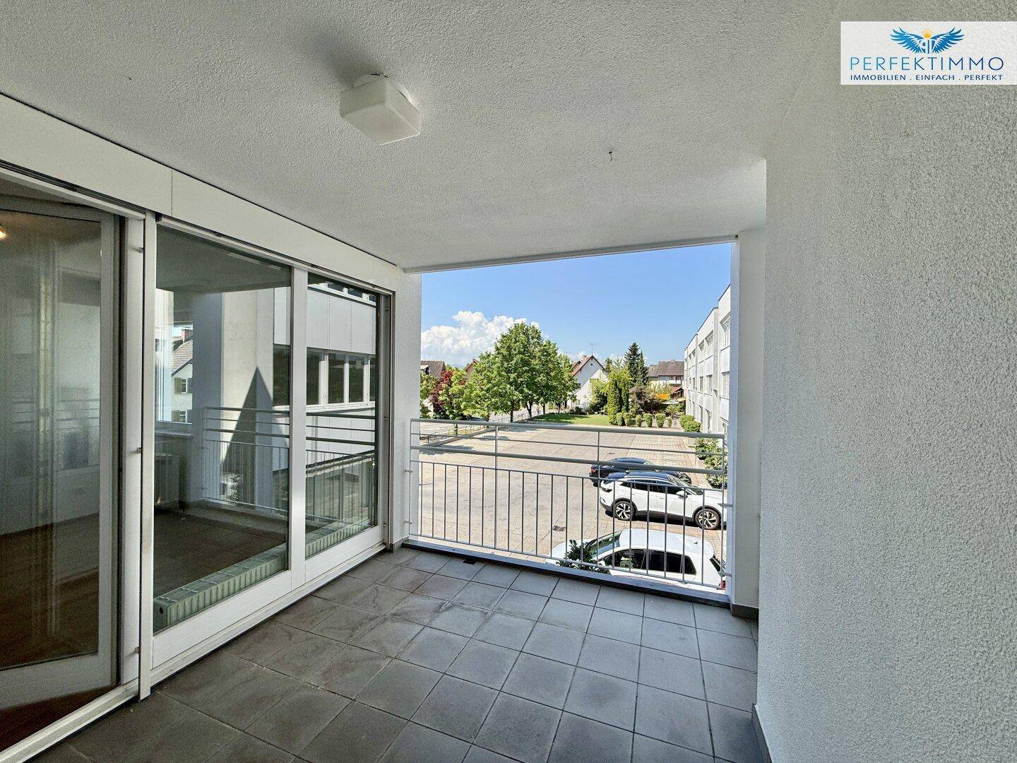Geräumiger Balkon mit Fliesenboden und Blick auf die umliegenden Gebäude und Bäume.