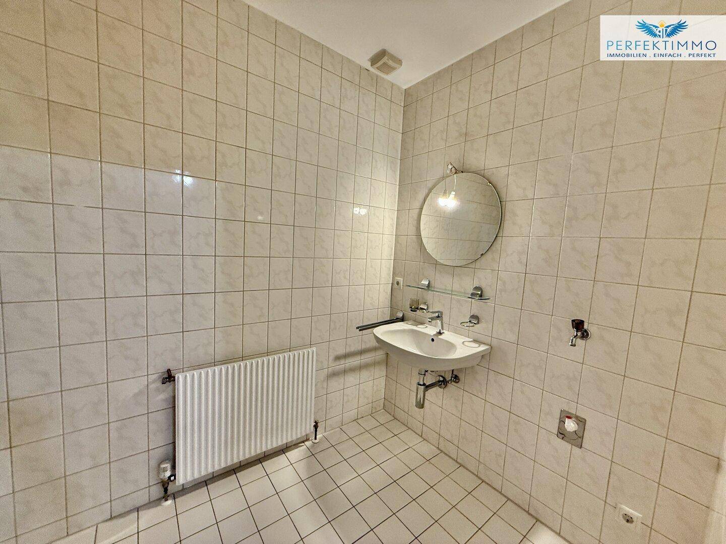 Gefliestes Badezimmer mit Waschbecken, Spiegel und Heizkörper, in gutem Zustand.