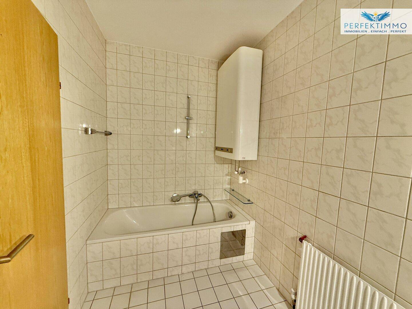 Helles Badezimmer mit Badewanne und Fliesen an Wänden und Boden.