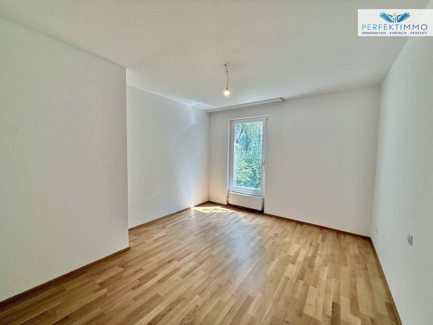 Helles Zimmer mit Parkettboden und Fenster, das viel Tageslicht hereinlässt.