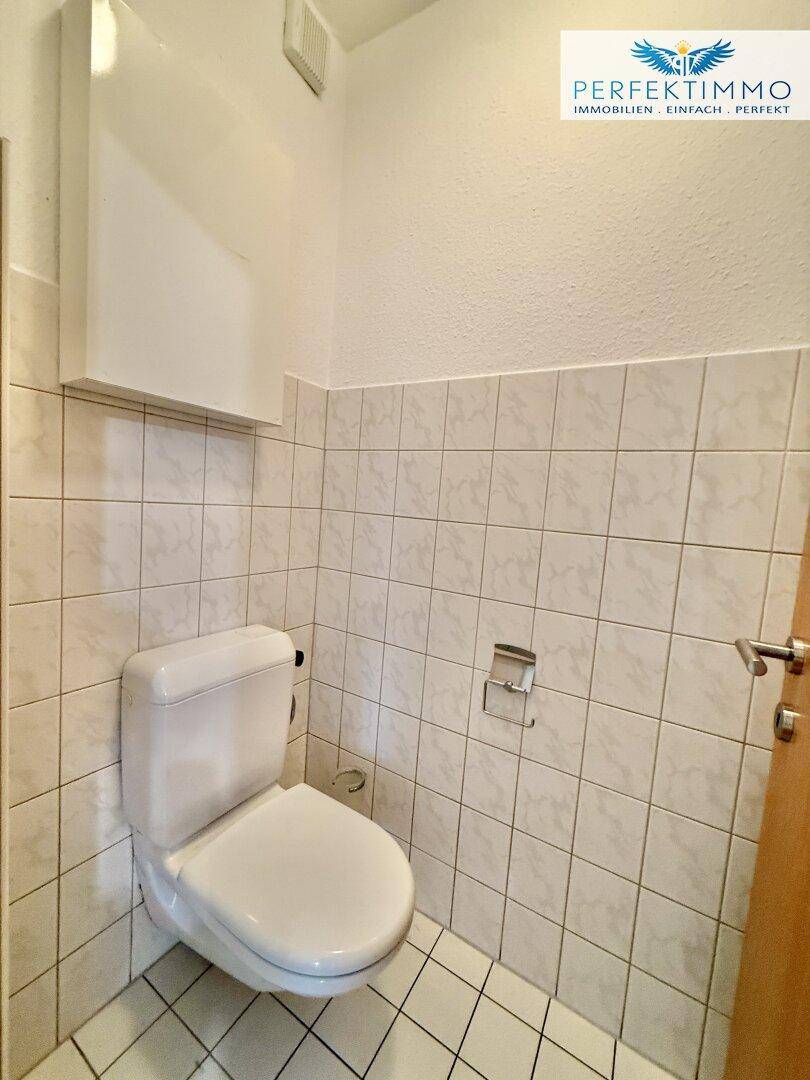 Separates WC mit Wand-WC und Fliesen an Wänden und Boden.
