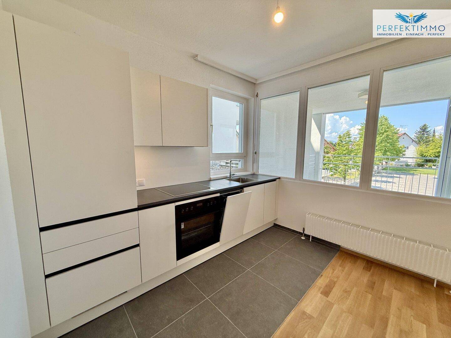 Moderne Einbauküche mit weißen Schränken, dunkler Arbeitsplatte und Fensterblick.