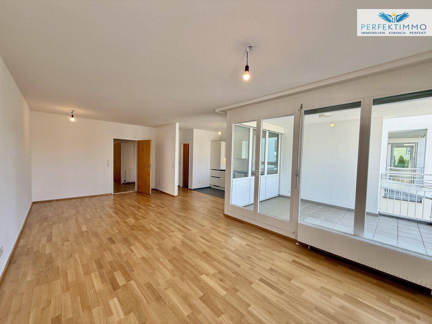 Weitläufiger Wohnbereich mit Parkettboden und großem Zugang zum Balkon.